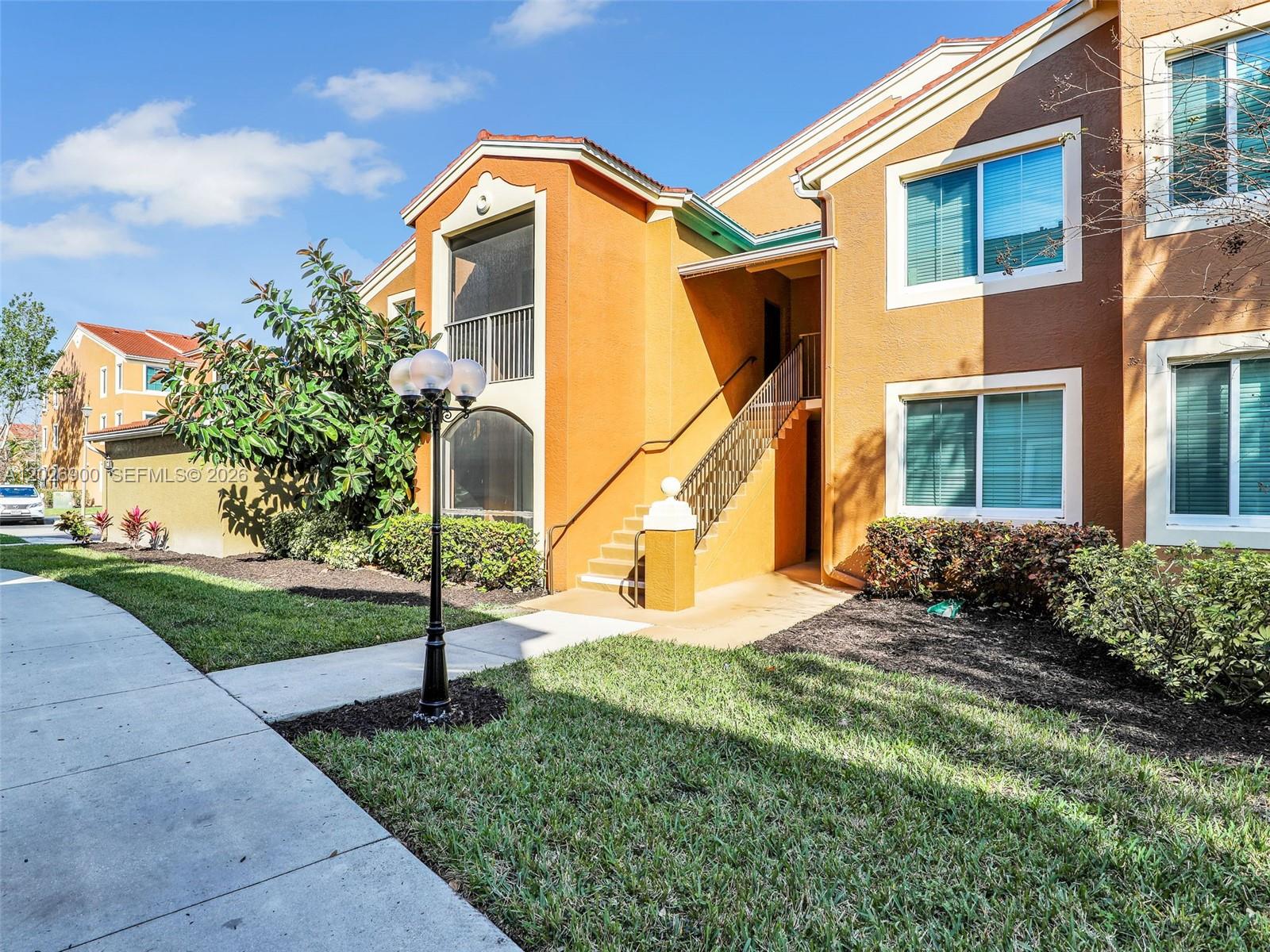 An exterior view of a two-story orange apartment building with stairs and a lamp post — 1235 Reserve Way # 107, Naples FL 34105, NAPLES, FL