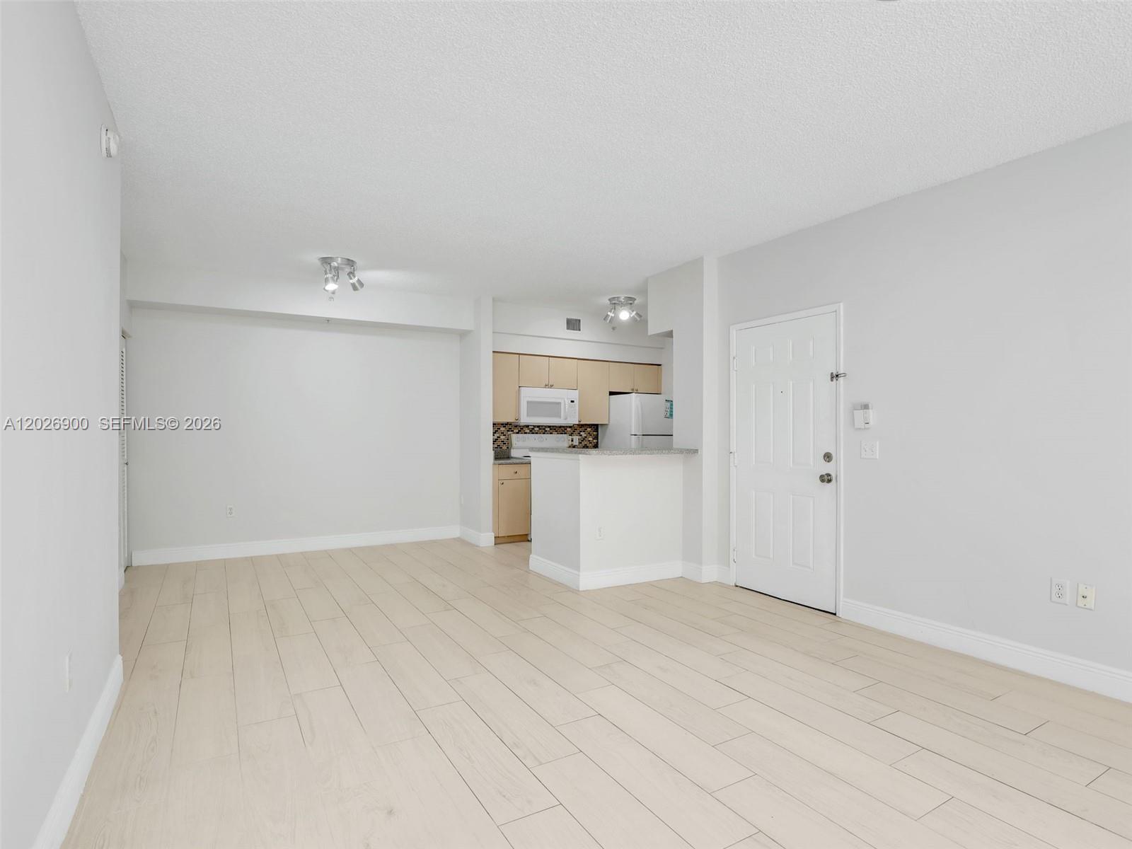 An open-concept living area features light wood-look tile flooring and an adjacent kitchen — 1235 Reserve Way # 107, Naples FL 34105, NAPLES, FL