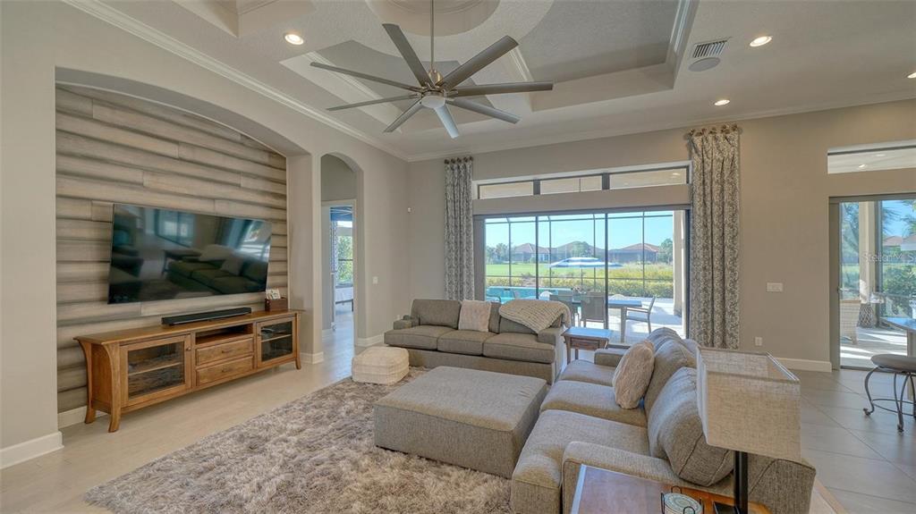 A living room features a wood-paneled accent wall, a large sectional sofa, and sliding doors — 4714 CABREO COURT, BRADENTON, FL