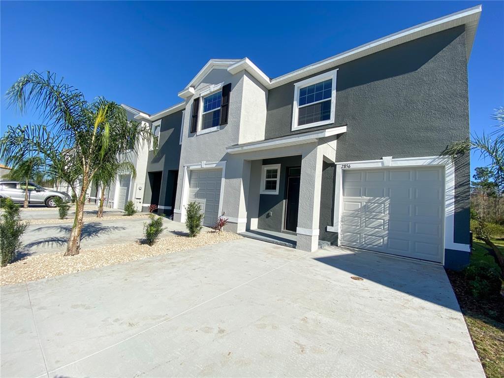 A two-story townhouse exterior with a gray stucco facade, white trim, and a concrete driveway — 2868 SUNCOAST BLEND DRIVE, ODESSA, FL