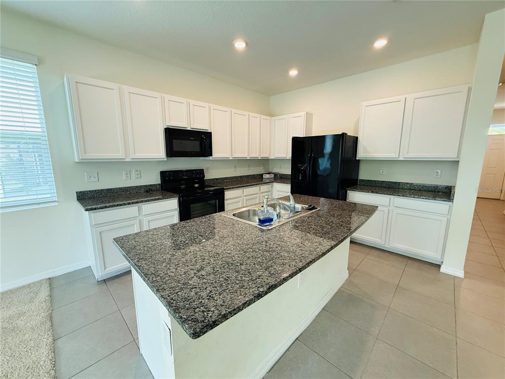 A kitchen features white cabinets, granite countertops, a center island, and black appliances — 2868 SUNCOAST BLEND DRIVE, ODESSA, FL