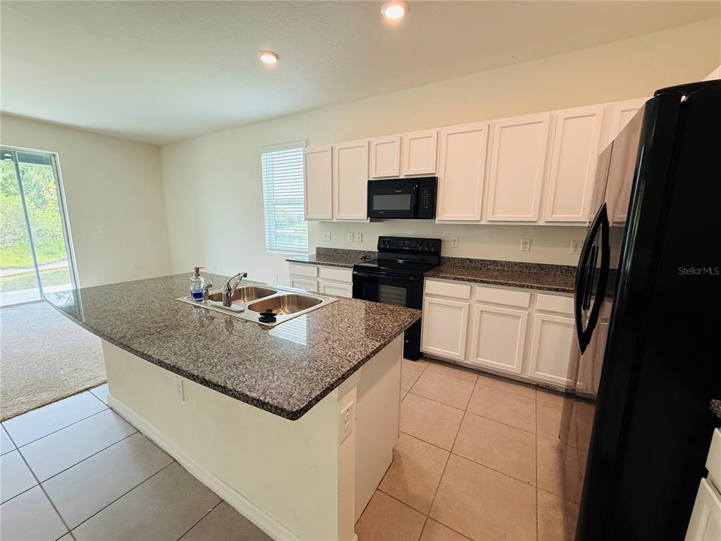 A kitchen features white cabinets, granite countertops, a center island, and black appliances — 2868 SUNCOAST BLEND DRIVE, ODESSA, FL