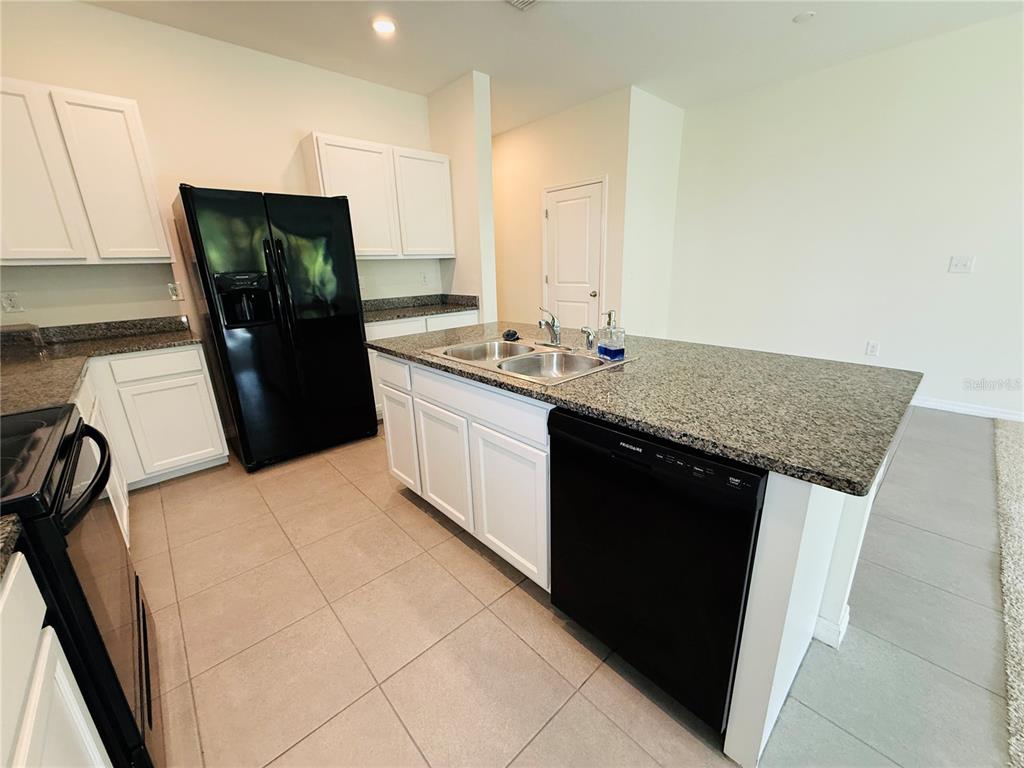 A kitchen features white cabinets, granite countertops, a black refrigerator, and a center island — 2868 SUNCOAST BLEND DRIVE, ODESSA, FL