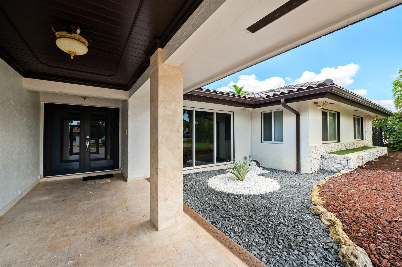 A covered entryway with stone flooring leads to a front door beside a rock garden — 2840 SW 128th Avenue, Miami FL 33175, MIAMI, FL