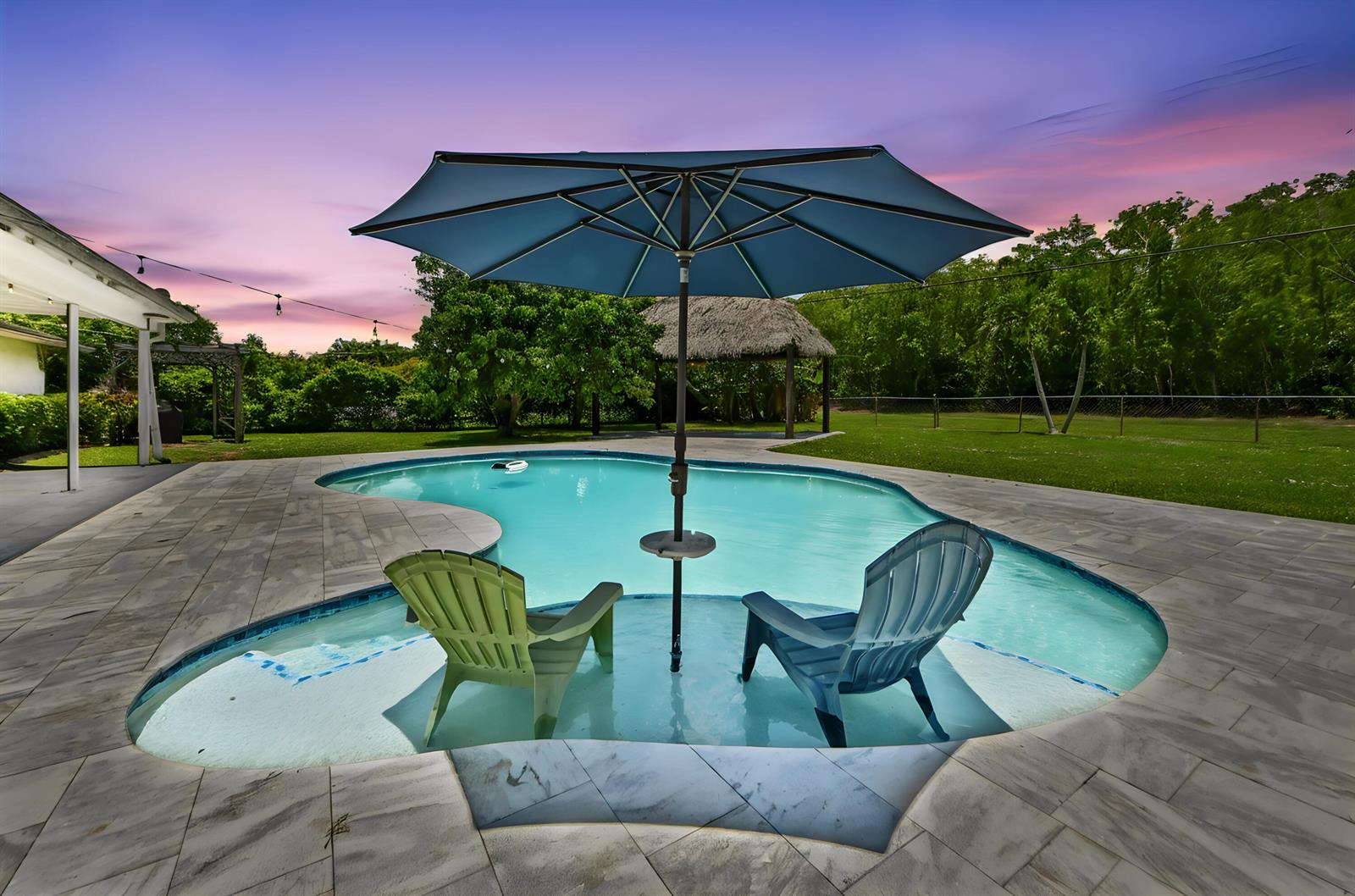 A swimming pool with a built-in sun shelf, two chairs, and an umbrella at sunset — 7635 Oakmont Drive, Lake Worth FL 33467, LAKE WORTH, FL