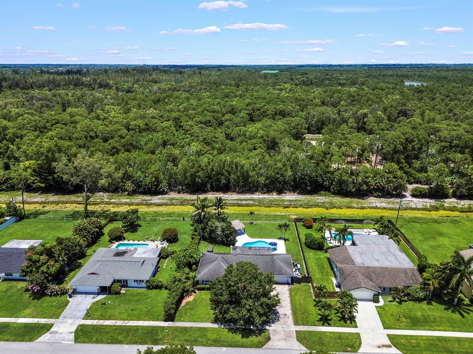 An aerial view shows three suburban houses with swimming pools bordering a large wooded area — 7635 Oakmont Drive, Lake Worth FL 33467, LAKE WORTH, FL