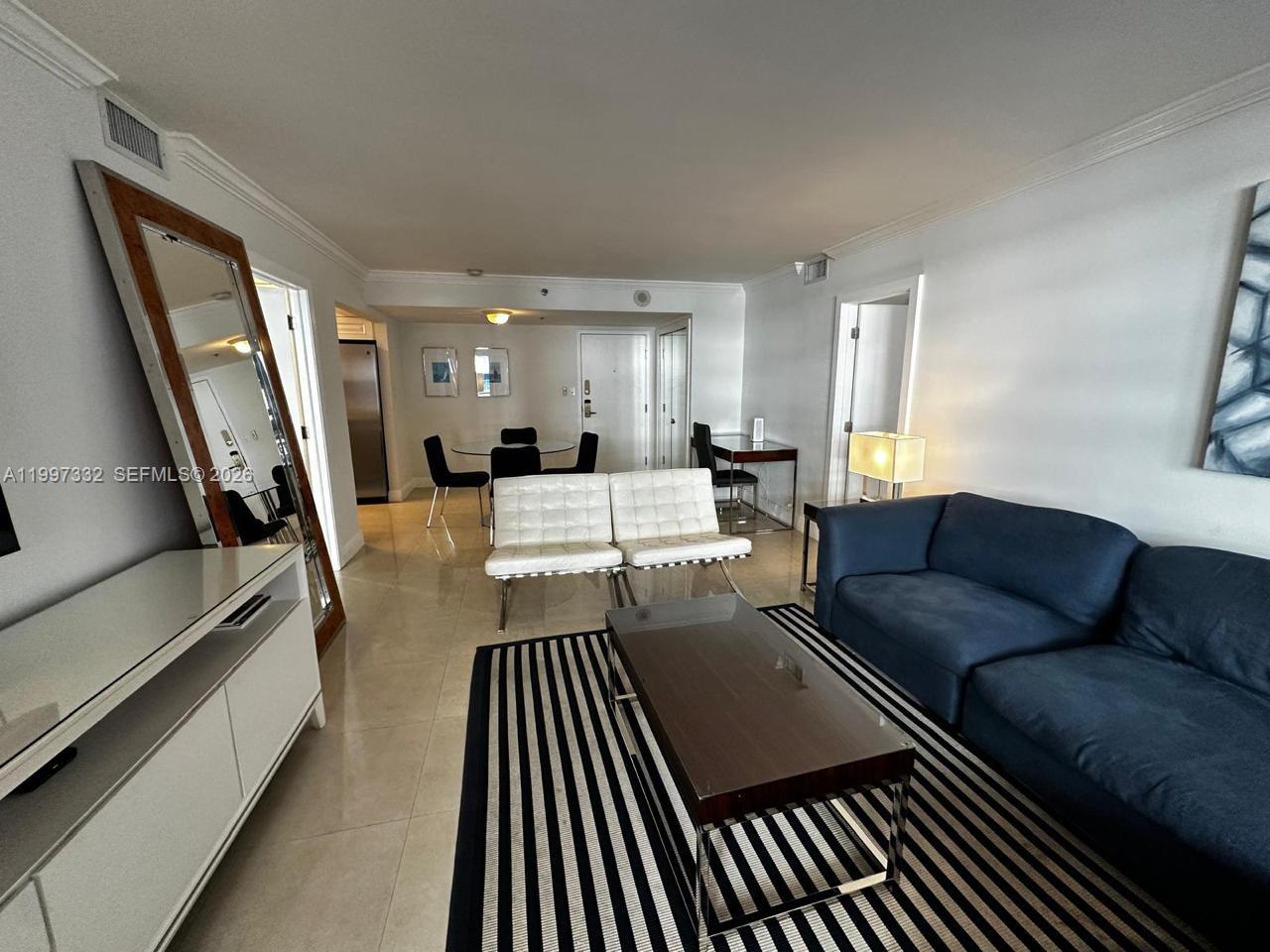 A living room features a blue sofa, a striped rug, and a white dining set — 5225 Collins Ave # 614, Miami Beach FL 33140, MIAMI BEACH, FL