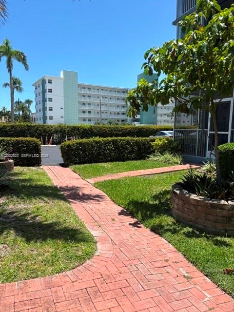 A brick walkway leads through a landscaped yard toward a multi-story apartment building — 3177 S Ocean Dr # 217, Hallandale Beach FL 33009, HALLANDALE BEACH, FL