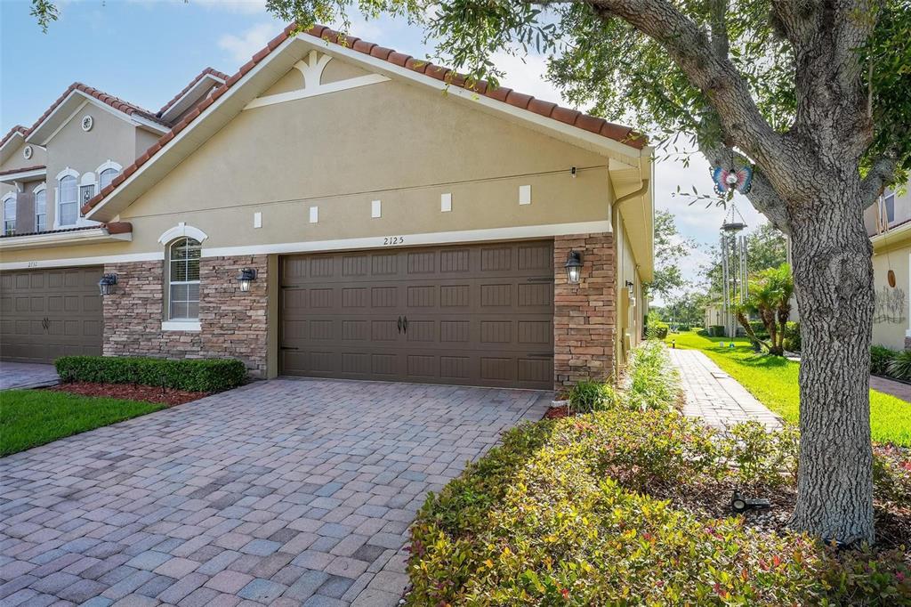 A tan stucco house with a stone facade, a brown garage door, and a paver driveway — 2125 VELVET LEAF DRIVE, OCOEE, FL