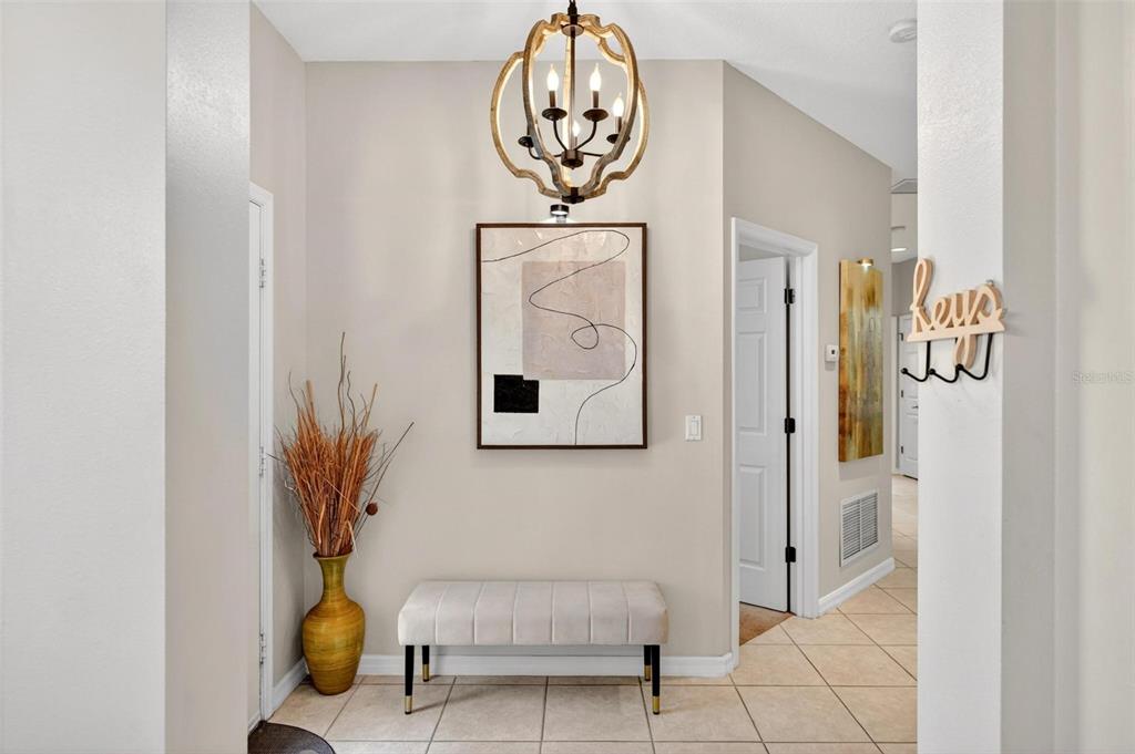 A foyer features a light-colored bench, abstract wall art, a chandelier, and tile flooring — 2125 VELVET LEAF DRIVE, OCOEE, FL