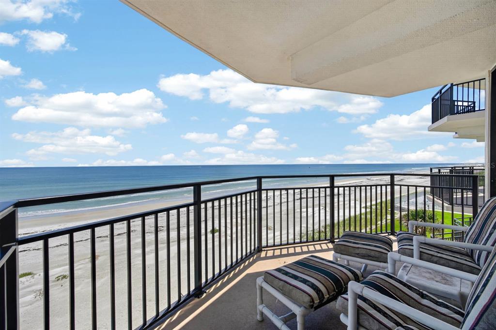 A balcony with striped chairs overlooks a sandy beach and the ocean under a blue sky — 4745 S ATLANTIC AVENUE UNIT 4050, PONCE INLET, FL