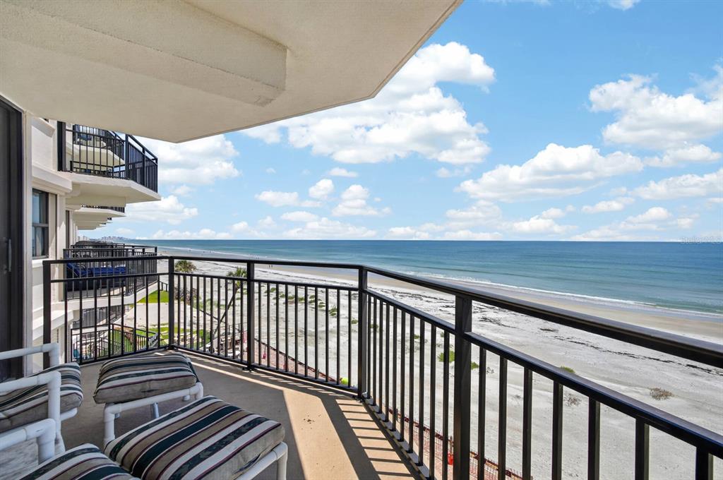 A balcony with striped chairs overlooks a sandy beach and the ocean under a cloudy sky — 4745 S ATLANTIC AVENUE UNIT 4050, PONCE INLET, FL