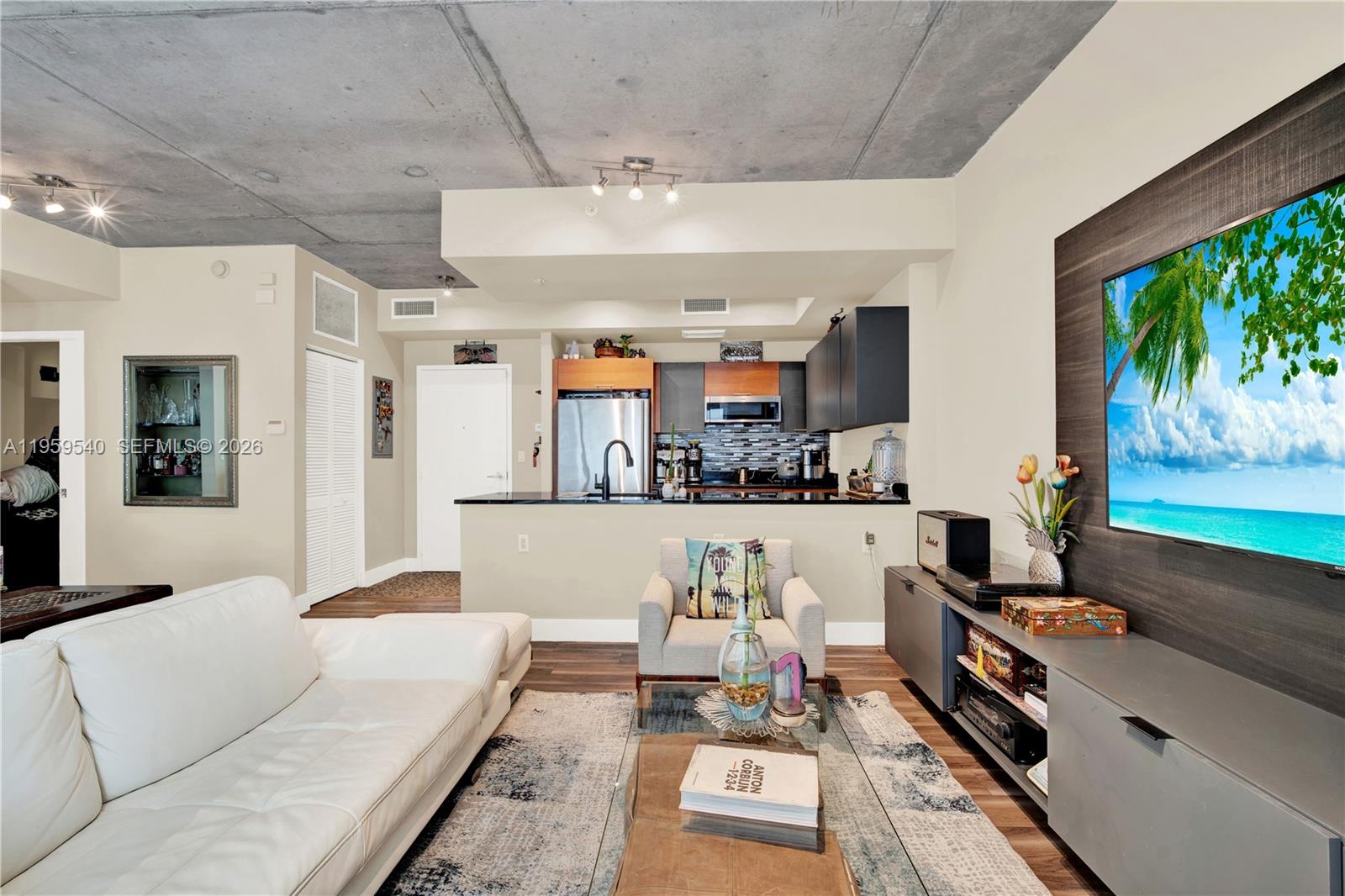 A living room with a concrete ceiling, white sofa, and an open kitchen in the background — 3449 NE 1st Ave # 110, Miami FL 33137, MIAMI, FL