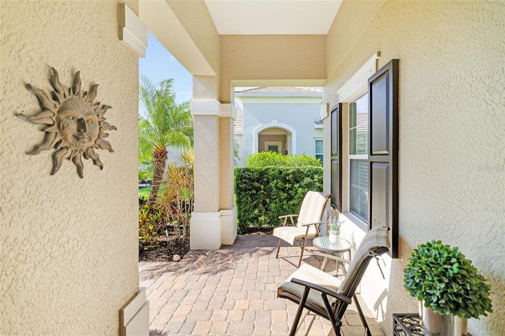 A covered patio features brick pavers, two chairs, a small table, and a sun wall decoration — 5437 CHATHAM SQUARE WAY, BRADENTON, FL