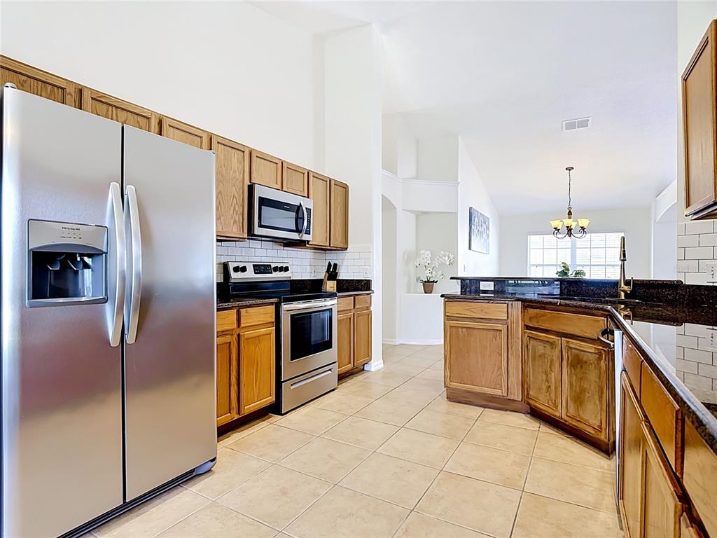 A kitchen with oak cabinets, stainless steel appliances, dark countertops, and light tile flooring — 7949 GOLDEN POND CIR, KISSIMMEE, FL