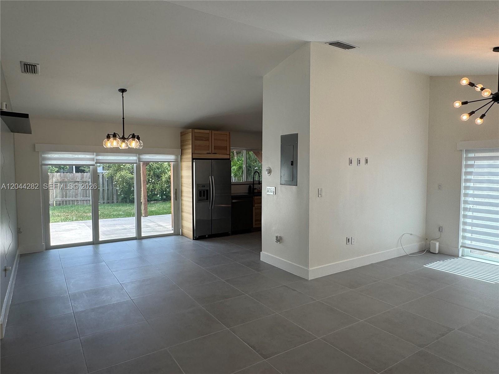 An open-concept living area features gray tile flooring, a kitchen with stainless appliances, and sliding doors — 12845 SW 150th Ter, Miami FL 33186, MIAMI, FL