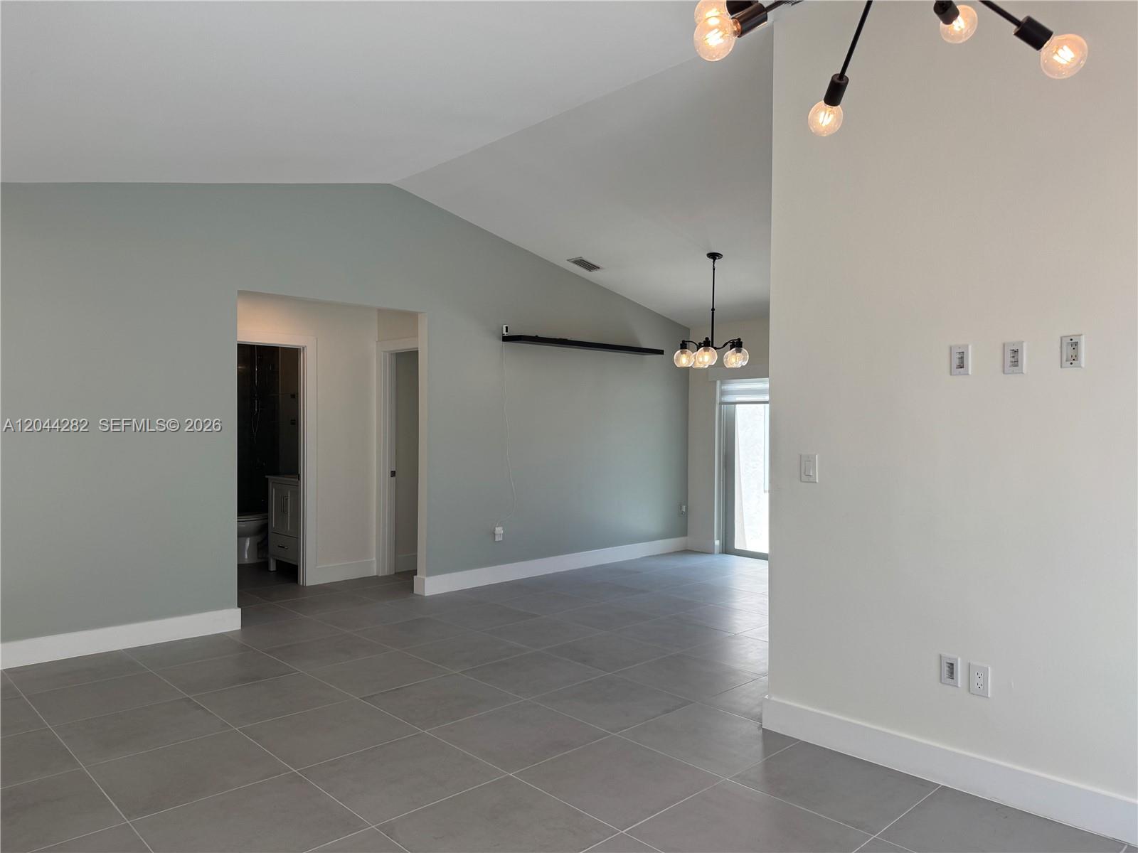 An open living area features vaulted ceilings, gray tile flooring, and two modern light fixtures — 12845 SW 150th Ter, Miami FL 33186, MIAMI, FL