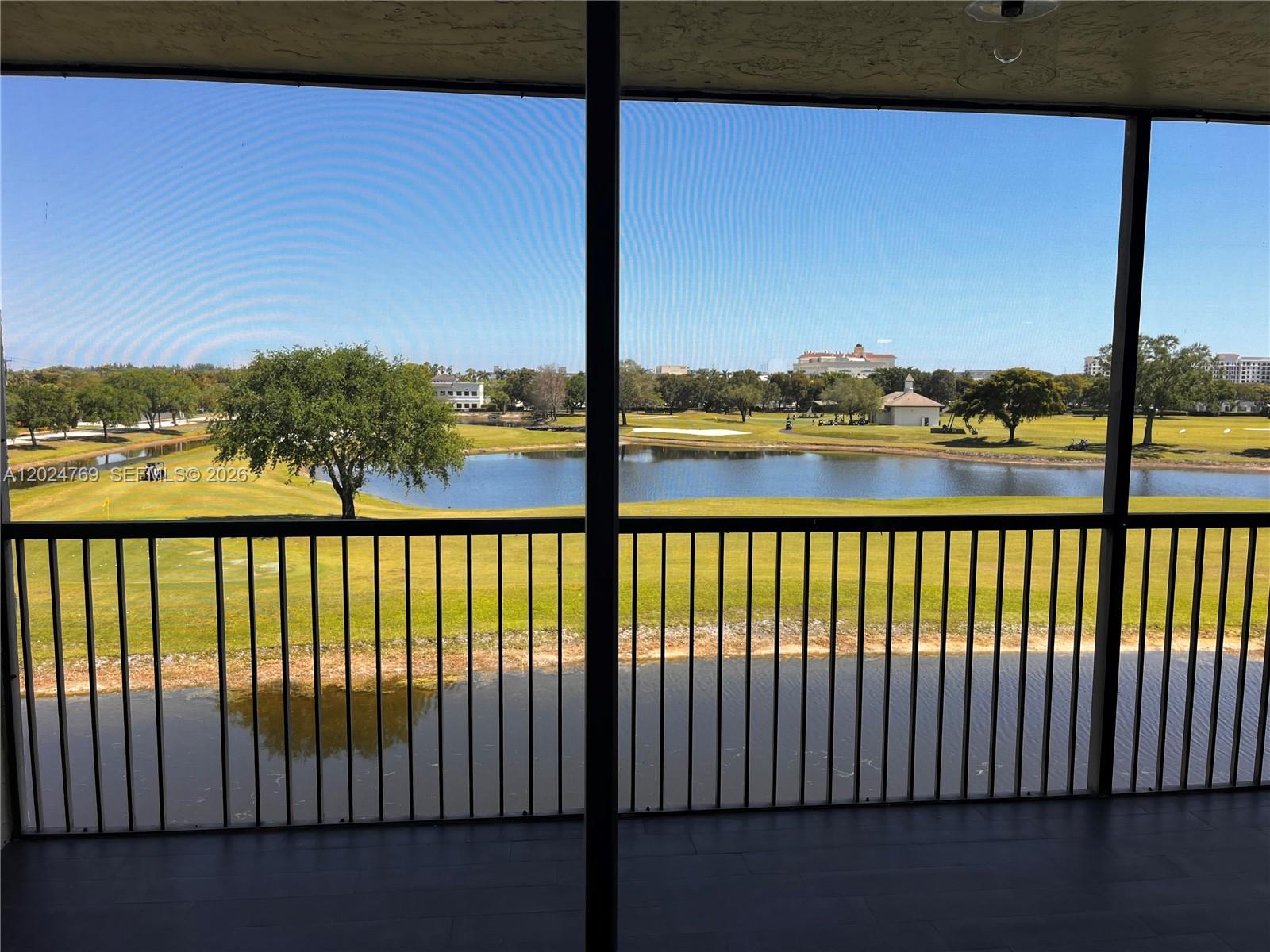 A screened-in balcony overlooks a pond and a golf course under a clear sky — 3100 W Rolling Hills Cir # 403, Davie FL 33328, DAVIE, FL