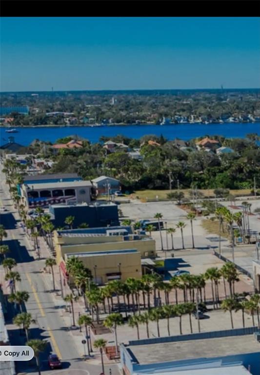 An aerial view shows a coastal street with palm trees, commercial buildings, and a nearby waterway — 11 N HOLLYWOOD AVENUE, DAYTONA BEACH, FL