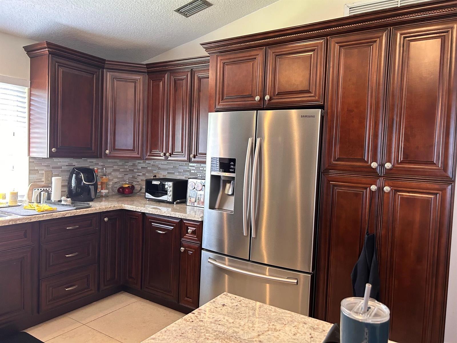 A kitchen features dark wood cabinetry, stainless steel appliances, and light granite countertops — 6754 Via Regina, Boca Raton FL 33433, BOCA RATON, FL