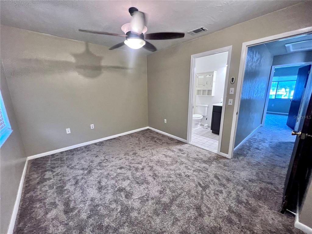 A bedroom with gray carpet, tan walls, a ceiling fan, and an attached bathroom — 2735 SW 35TH PLACE UNIT 2004, GAINESVILLE, FL