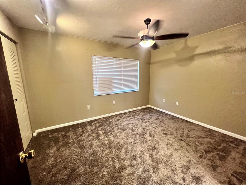 An empty bedroom features dark brown carpeting, tan walls, a ceiling fan, and a window — 2735 SW 35TH PLACE UNIT 2004, GAINESVILLE, FL