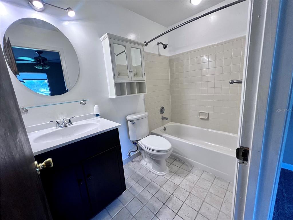 A bathroom features a dark vanity, a round mirror, a toilet, and a tiled tub-shower — 2735 SW 35TH PLACE UNIT 2004, GAINESVILLE, FL