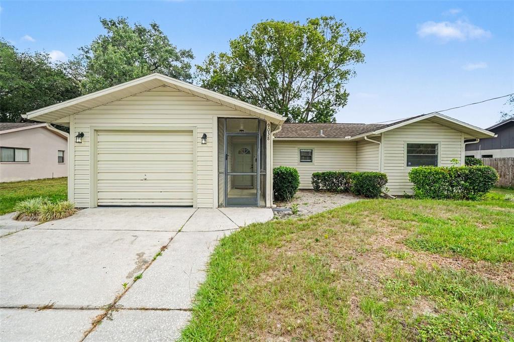 A single-story house with beige siding, a one-car garage, and a front screen door — 9038 BLACKSTONE STREET, SPRING HILL, FL