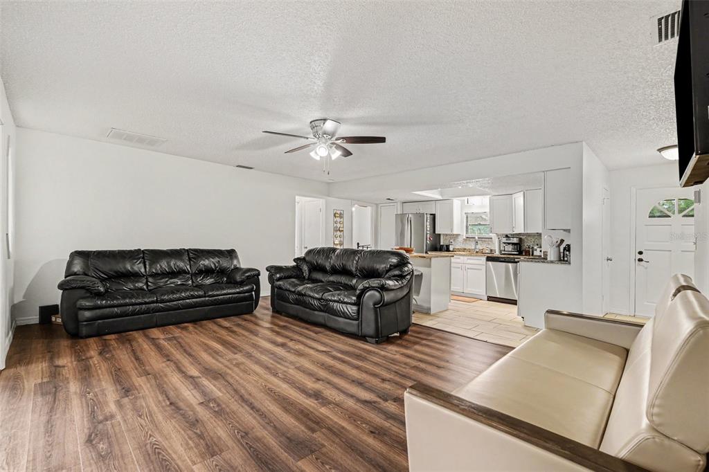 A living room with wood-look flooring, two black leather sofas, and an open-concept kitchen — 9038 BLACKSTONE STREET, SPRING HILL, FL