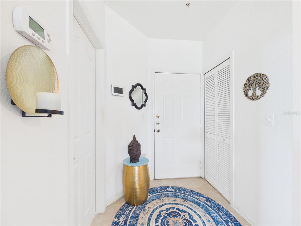 A bright entryway features a white door, a closet with louvered doors, and a round rug — 8816 DUNES COURT UNIT 302, KISSIMMEE, FL