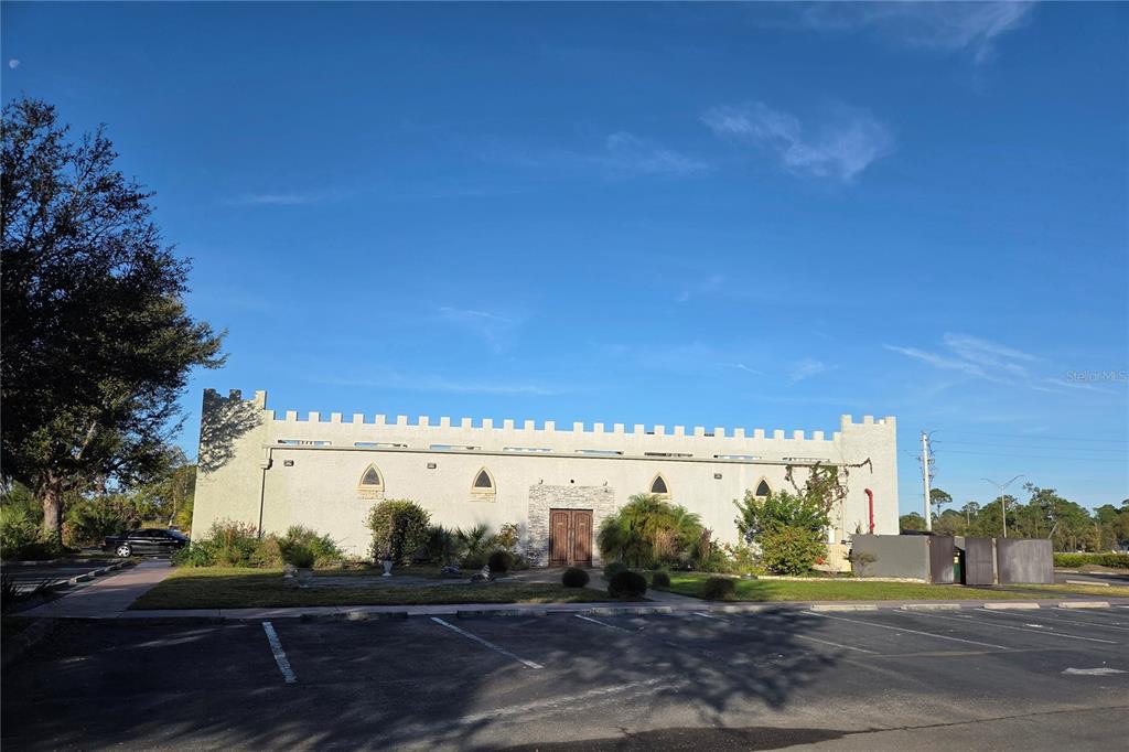 A light-colored building with crenellated roofline parapets stands behind a large asphalt parking lot — 23507 SPENCER COURT, PUNTA GORDA, FL