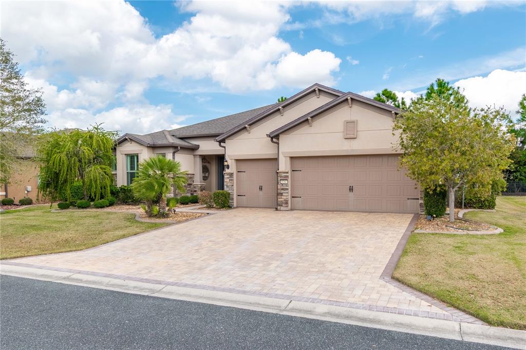 A single-story house with a beige stucco exterior, stone accents, and a paved driveway — 9761 SW 74TH PLACE, OCALA, FL