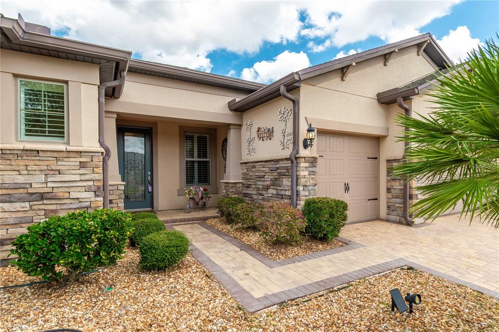 A single-story house exterior features a stone facade, a paved walkway, and a garage — 9761 SW 74TH PLACE, OCALA, FL
