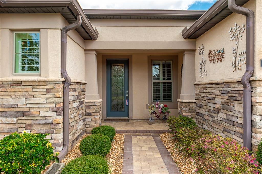 A stone-accented home exterior features a paved walkway leading to a glass-paneled front door — 9761 SW 74TH PLACE, OCALA, FL