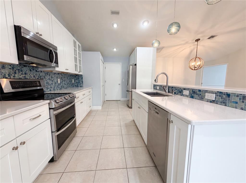 A kitchen features white cabinetry, stainless steel appliances, a blue mosaic backsplash, and tile flooring — 4816 61ST AVENUE TERRACE W, BRADENTON, FL