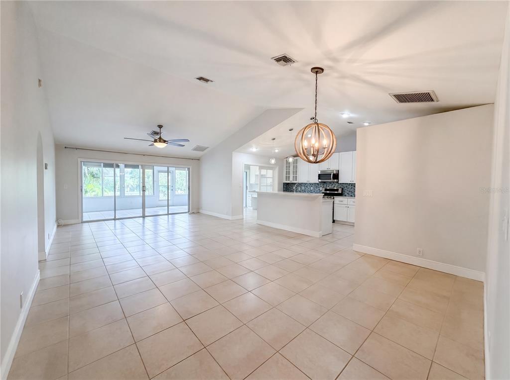 An open-concept living area features tile flooring, a kitchen with white cabinetry, and sliding doors — 4816 61ST AVENUE TERRACE W, BRADENTON, FL