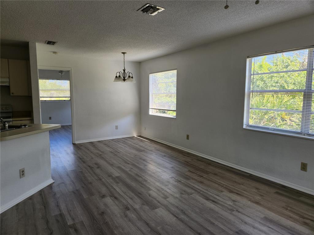 A dining area with wood-look flooring, a chandelier, and two windows overlooking greenery — 9522 ACE ROAD UNIT B, ENGLEWOOD, FL