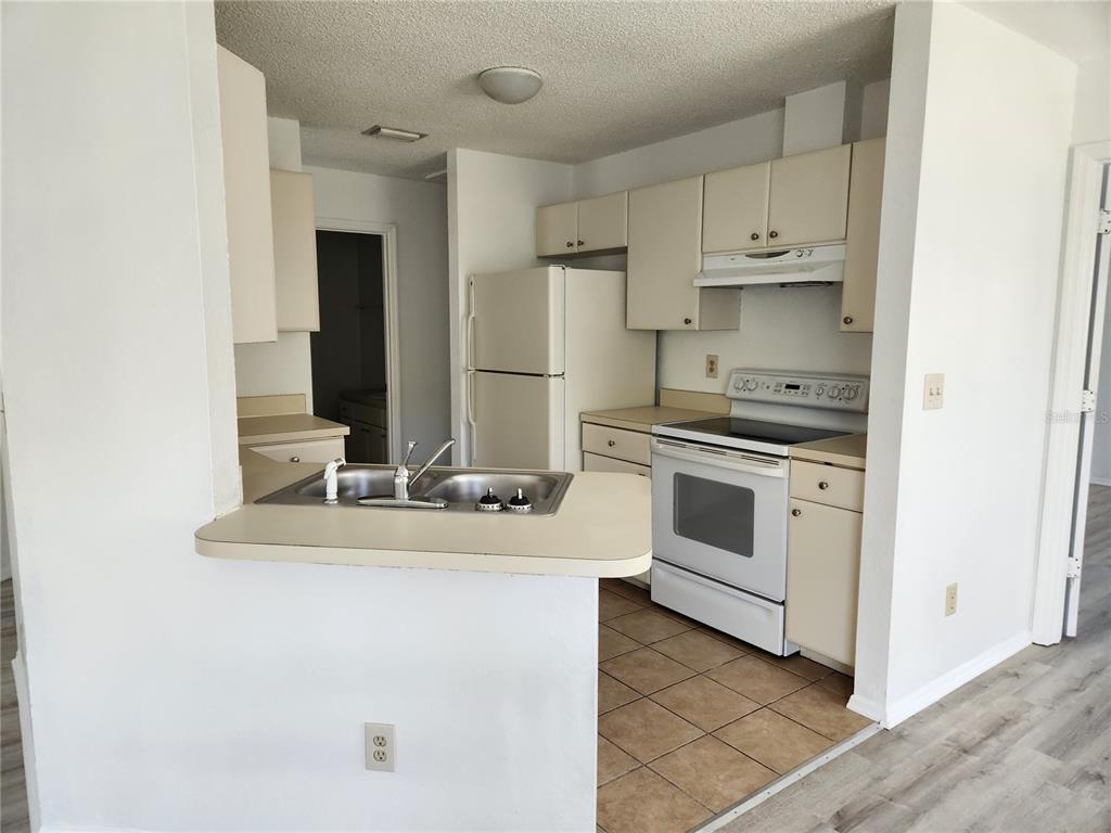 A kitchen with white cabinets, white appliances, a double sink, and tan tile flooring — 9522 ACE ROAD UNIT B, ENGLEWOOD, FL