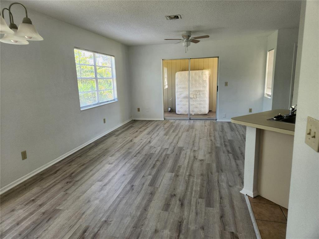An empty living room features light gray wood-look flooring, a ceiling fan, and sliding doors — 9522 ACE ROAD UNIT B, ENGLEWOOD, FL
