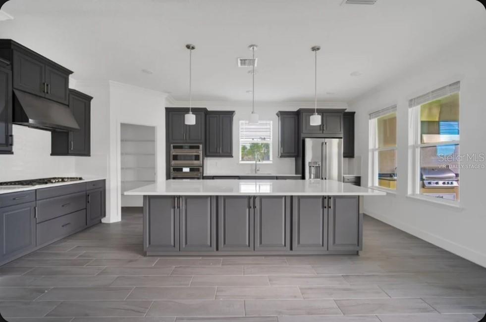 A kitchen with dark gray cabinets, a large white island, and light wood-look tile floors — 15997 HONEY HARVEST STREET, WINTER GARDEN, FL