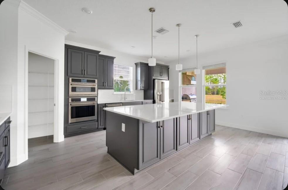 A kitchen with dark gray cabinets, a large white island, and light wood-look tile flooring — 15997 HONEY HARVEST STREET, WINTER GARDEN, FL