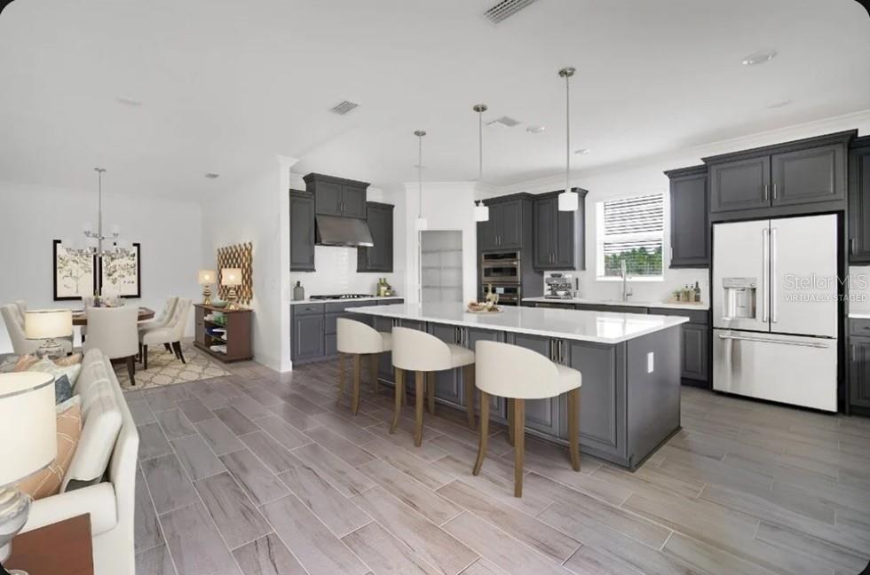 A kitchen with dark gray cabinets, a white island, and light wood-look tile flooring — 15997 HONEY HARVEST STREET, WINTER GARDEN, FL