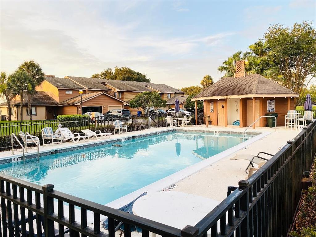 A rectangular swimming pool is surrounded by a black metal fence and a pool house — 707 CARPENTERS WAY UNIT 8, LAKELAND, FL