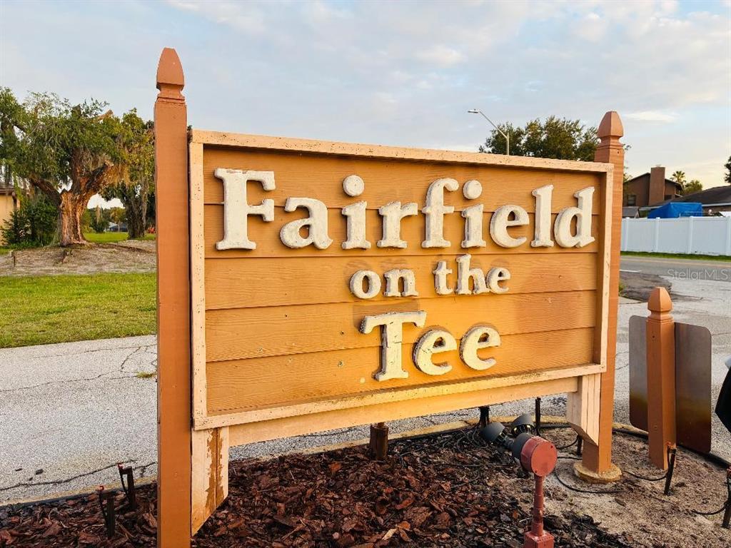 A wooden sign for Fairfield on the Tee stands outdoors near a paved road — 707 CARPENTERS WAY UNIT 8, LAKELAND, FL