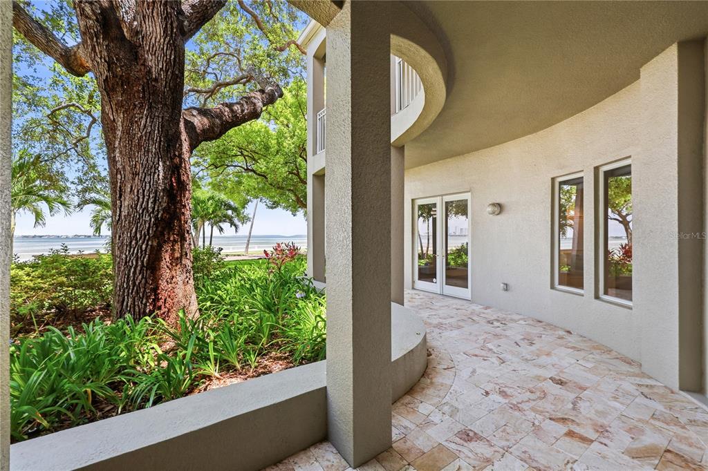 A curved stone patio overlooks a garden and a body of water under a large tree — 3507 BAYSHORE BOULEVARD UNIT 102, TAMPA, FL