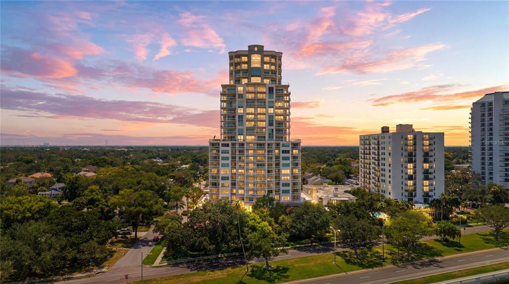 An aerial view of a tall residential tower surrounded by trees at sunset — 3507 BAYSHORE BOULEVARD UNIT 102, TAMPA, FL