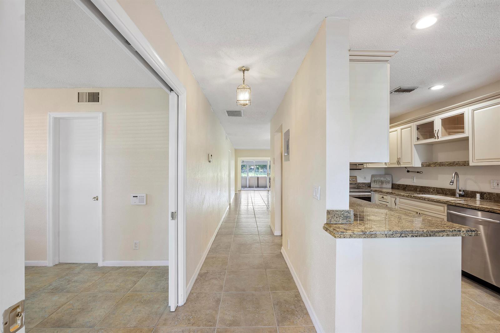 A hallway with tile flooring leads toward a glass door, flanked by a kitchen and room — 1020 Citrus Way # 101, Delray Beach FL 33445, DELRAY BEACH, FL