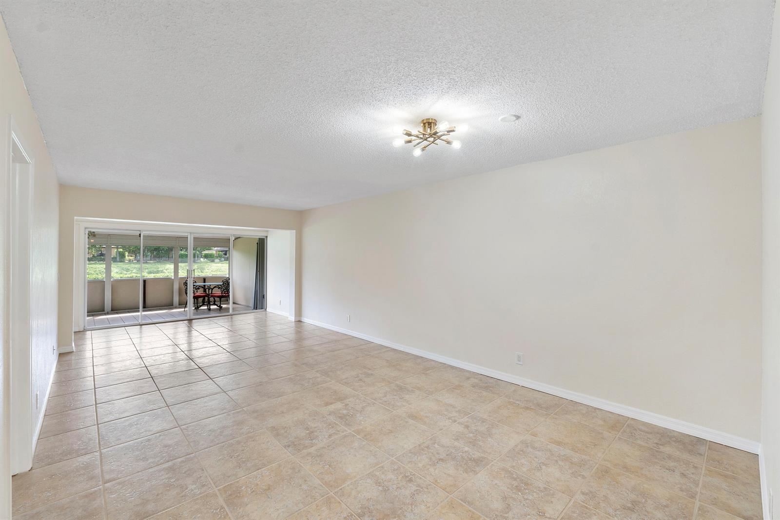 An empty living room features beige tile flooring, a central light fixture, and sliding glass doors — 1020 Citrus Way # 101, Delray Beach FL 33445, DELRAY BEACH, FL