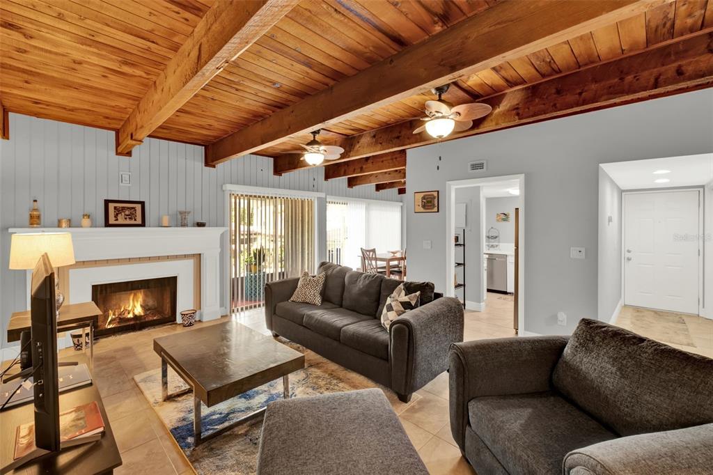 A living room features a fireplace, wood-beamed ceiling, and dark gray furniture on tile flooring — 105 FAIRWAY DRIVE, LONGWOOD, FL