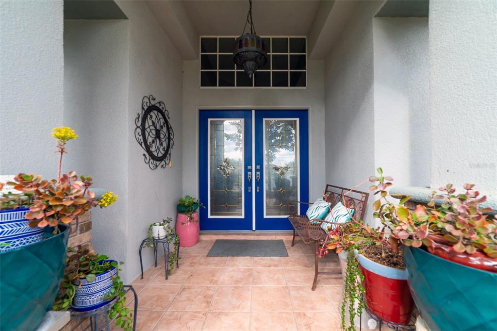 A covered entryway features double blue doors, tiled flooring, potted plants, and a metal bench — 4347 GEVALIA DRIVE, BROOKSVILLE, FL
